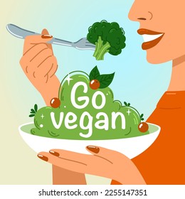  A woman holds a fork of broccoli in one hand and a plate with the inscription go vegan in the other hand