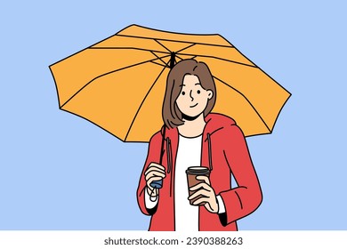 Woman holds plastic cup with coffee takeouts and umbrella protecting from rain during autumn walk. Girl enjoys taste of invigorating takeouts coffee and looks at screen with thoughtful grin.