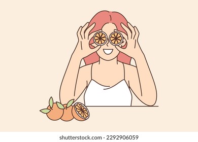 Woman holds slices of citrus fruit near eyes offering to use orange for rejuvenating facial mask. Girl uses fruits of citrus tree to prepare breakfast with detox effect and useful vitamins 