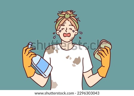 Woman housewife in dirty clothes is crying because of large amount housework and lack of rest. Girl housewife with tears in eyes holds sponge and spray bottle for cleaning in apartment