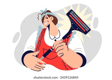 Woman housewife holds vacuum cleaner and smiles slyly looking at screen, dressed in apron for housework. Girl maid uses vacuum cleaner to clean dust in apartment and take care of cleanliness of rooms.