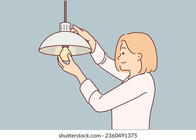 La mujer cambia de forma independiente la bombilla de luz quemada para lograr una iluminación de alta calidad en la casa. Chica con sonrisa inserta bombilla de luz en la lámpara colgando debajo del techo, sin ayuda de electricista