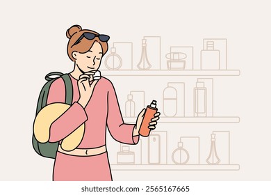 Woman inhales aroma of perfume, stands near counter of store selling cosmetics and expensive perfume. Girl selects appropriate scent to highlight look for going to party and attract attention of men.