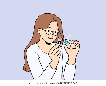 Woman jeweler examines gemstone through magnifying glass, checking diamond for authenticity. Girl enjoys appearance of diamond and studies emerald under loupe, before creating ring or necklace