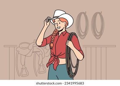 Woman jockey stands in stable wearing cowboy hat and holding long rope waiting for horses to appear. Girl rancher dressed in cowgirl style smiling when you cheer for jockey at races