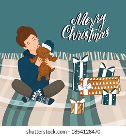 Woman in knitted new year socks and hoodie with cat or kitten in the room on bed with plaid and Merry Christmas text on the wall and bought gifts