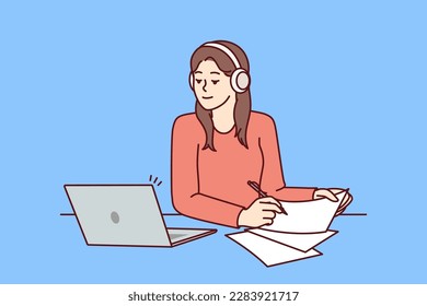 Woman with laptop sits at table and watches training webinar for gaining new skills and makes notes on paper. Attentive girl in headphones using laptop to get online education at university or college