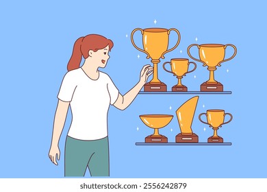 Woman leader stands near gold awards and cups won in sports competitions or professional competitions. Girl leader is proud to have trophies earned for outstanding results in business