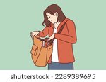 Woman looks into large bag hanging on shoulder in search of wallet or phone lost in handbag. Tourist girl with handbag dressed in casual clothes is trying to find lost or stolen personal items. 