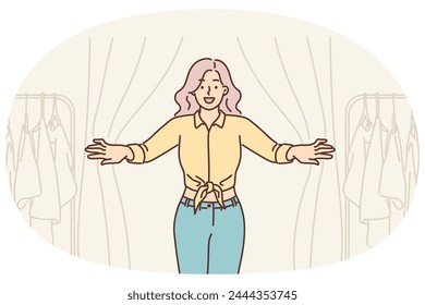 Woman looks out of fitting room in clothing store while shopping and choosing new look. Hipster girl stands in fitting room near hangers with t-shirts for everyday wear or dresses for party