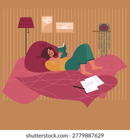 A woman is lying on a bed reading a book with a notebook beside her