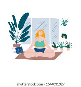 Woman is meditating on yoga mat at home. House plants near the window, urban jungle. 