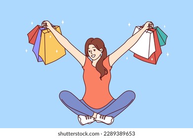 Woman with multi-colored packages from clothing stores sits with her arms apart after successful shopping. Girl who won shopping lottery shows off things purchased at big discount or cashback 