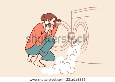 Woman near broken washing machine calls home electronics repairman because of foam pouring out of drum. Excited housewife sitting looking at washing machine with factory defect causing leak