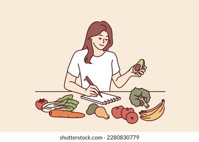 Woman near table with vegetables makes notes in notebook counting calories or making plan for new keto diet. Girl takes care of diet by choosing only organic vegetables grown by farmers 