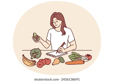 Woman near table with vegetables makes notes in notebook counting calories or making plan for new keto diet. Girl takes care of diet by choosing only organic vegetables grown by farmers