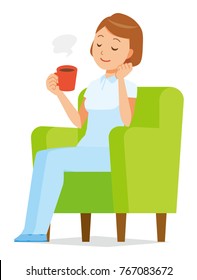 A woman nurse in a white uniform sits on a sofa and is drinking coffee