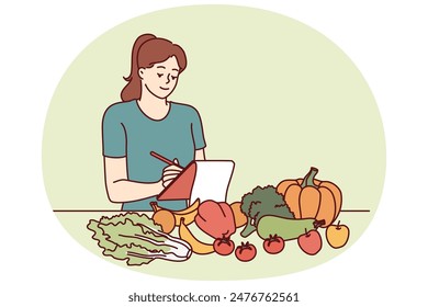 Woman nutritionist is standing near table with vegetables and making notes in notebook, making plan for new diet to detoxify body. Girl nutrition specialist uses checklist to mark diet ingredients