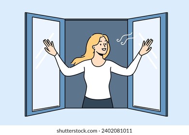 Woman opens window enjoying fresh air coming from street into apartment, and smilingly looks at passers-by. Girl stands near window and wants to check room to get rid of unpleasant smell in house.