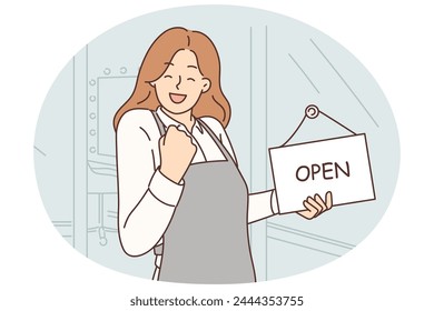 Woman owner of beauty salon makes victory gesture standing near front door with sign open on day of business launch. Girl stylist opens own business wanting to become successful entrepreneur