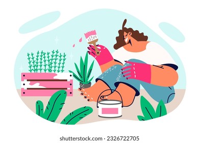 Woman painting garden furniture with plants sitting on ground and making DIY decorations for backyard of own house. Girl works as florist and changes color of wooden box for plants from garden