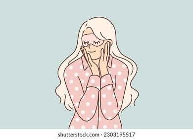 Woman in pajamas and sleep mask smiles getting ready for night rest after hard day work. Young blonde girl dressed in pajamas applies anti-wrinkle cream on face before going to bed