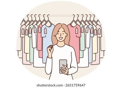 Woman with phone near hanger with T-shirts rejoices in sale and opportunity to buy clothes at discounts. Girl uses smartphone for bargain shopping through online application with discounts
