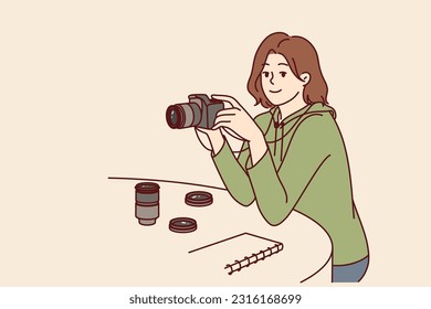 Woman photographer with camera sits at table choosing lens for photo essay or creating portrait of interlocutor. Girl with camera works as newspaper photographer taking pictures for news publications.