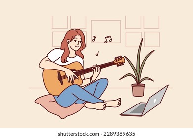 Woman plays guitar sitting in front of laptop and gets musical skills from watching video lesson on internet. Girl enjoys musical hobby and performance of popular compositions on guitar 