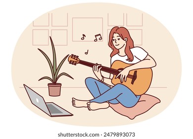 Woman plays guitar sitting in front of laptop and gets musical skills from watching video lesson on internet. Girl enjoys musical hobby and performance of popular compositions on guitar