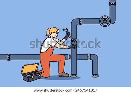 Woman plumber repairs pipes in factory, using wrench to fix crack in industrial pipeline. Girl in overalls works as plumber, easily doing men job and enjoying difficult profession.