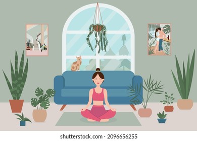 A woman practices yoga in a lotus position in a cozy room with a large window, potted plants and a cat.