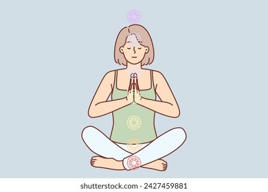 Woman practices yoga sitting in lotus position to cleanse aura and activate chakras to achieve perfection. Young girl folds hands in front of chest while meditating and doing yoga.