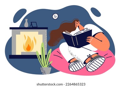 Woman is reading book enjoying interesting plot and sitting in easy chair near fireplace. Girl reading book in comfortable home environment studies professional literature to gain new skills