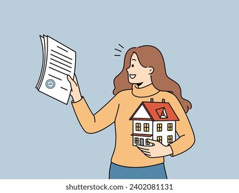 Woman realtor helps people in purchasing real estate and holds mortgage contract and model of house in hand. Realtor girl smiles, rejoicing at selling house and receiving percentage for work.