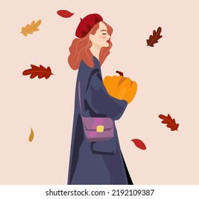 A woman with red hair in a coat and a red take is holding a pumpkin in her hands. Coloured leaves in the background. The autumn concept is suitable for the avatar of the social network.