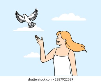 Woman releases dove standing under summer blue sky and watching bird symbolize hope and peace. Happy girl looks with smile at dove soaring in sky and enjoys communicating with nature