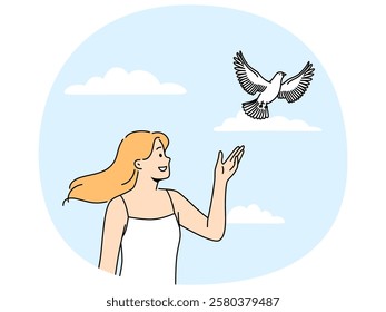 Woman releases dove standing under summer blue sky and watching bird symbolize hope and peace. Happy girl looks with smile at dove soaring in sky and enjoys communicating with nature