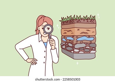 Woman scientist with magnifying glass is engaged in geology in search of deposits of valuable resources. Girl ecologist in white coat conducts examination of soil pollution