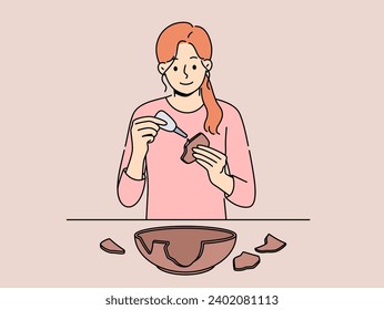 Woman seals broken clay plate to hide carelessness or demonstrate conscious consumption. Girl archaeologist with smile uses glue restoring clay dishes found at excavations for display in museum.