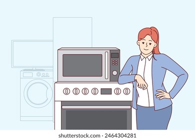 Woman selling household appliances stands near oven and washing machine and looks at camera. Girl smiles and rejoices in purchasing new home appliances with IOT wifi synchronization technology