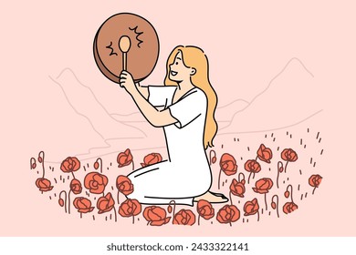 Woman shaman with drum sits in poppy field and plays ethnic musical instrument to bring about rain. Girl shaman observes mystical traditions of calling gods on days of spring equinox