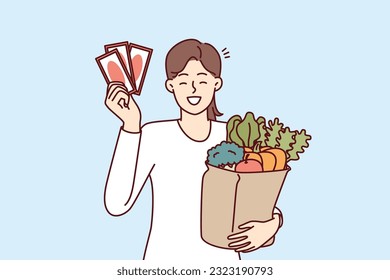 Compradora de mujeres con vales de regalo de supermercado y bolsa de papel llena de verduras frescas. Muchacha feliz mostrando cupones de descuento o cupones para comprar en una tienda de comestibles a precios de ganga