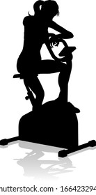A woman in silhouette using a stationary exercise spin bike piece of gym equipment fitness machine 