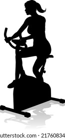 A woman in silhouette using a stationary exercise spin bike piece of gym equipment fitness machine 