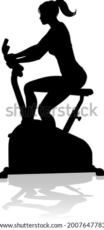 A woman in silhouette using a stationary exercise spin bike piece of gym equipment fitness machine 