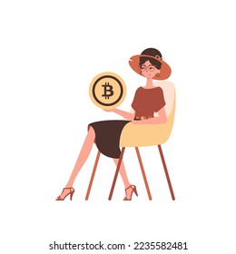 A woman sits in a chair and holds a bitcoin coin in her hands.