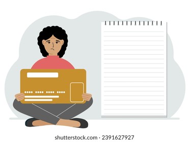 A woman sits cross-legged in his hands holding a large credit card next to a close-up notepad for text. Concept of credit card, expense planning, income planning.
