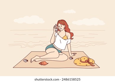 Woman sits on beach and listens to sound of sea from shell, enjoying summer vacation at tropical resort. Tourist girl sunbathes on beach of paradise island in ocean during weekend.