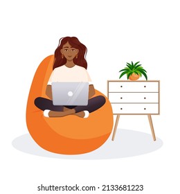 Woman sits on the bean bag chair and works at the computer. Remote work, office at home, programming, freelance. Study at home in quarantine. Vector illustration.